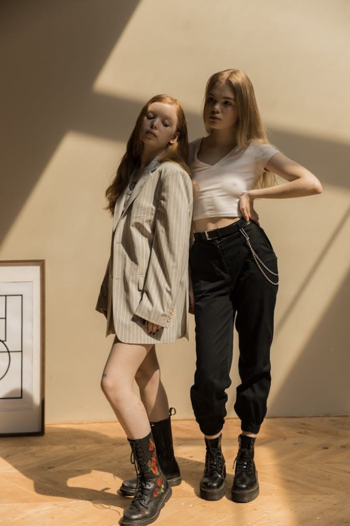 Two stylish caucasian women in trendy outfits posing indoors with creative shadows.