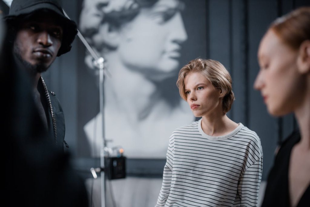 Three models in a fashion photoshoot with blurred classical sculpture background in a studio.